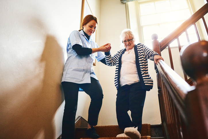 Nursing home staff member helping an elderly woman down the stairs